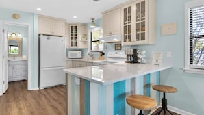 A kitchen with a central island, white cabinets, a microwave, a coffee maker, and a window with blinds. - Beachwood Villas (Santa Rosa Beach)
