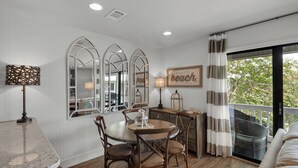 A dining area with a round table, chairs, and a chandelier. There are three large mirrors on the wall, a lamp, and a sign that says "beach". - Beachwood Villas (Santa Rosa Beach)