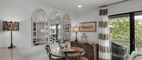 A dining area with a round table, chairs, and a chandelier. There are three large mirrors on the wall, a lamp, and a sign that says "beach".