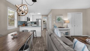 A modern kitchen with white cabinets, a stainless steel refrigerator, and a dining area with a wooden table and bar stools. - Beachwood Villas (Santa Rosa Beach)
