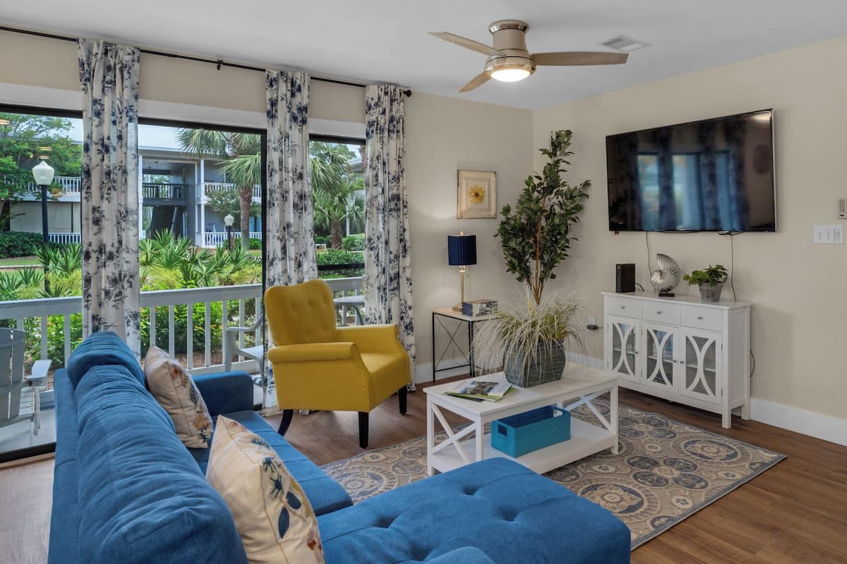 Una sala de estar con un sofá azul, un sillón amarillo y un mueble blanco con un televisor encima.