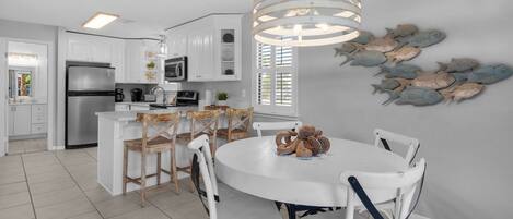 A modern kitchen with white cabinetry, a stainless steel refrigerator, and a round dining table with white chairs.