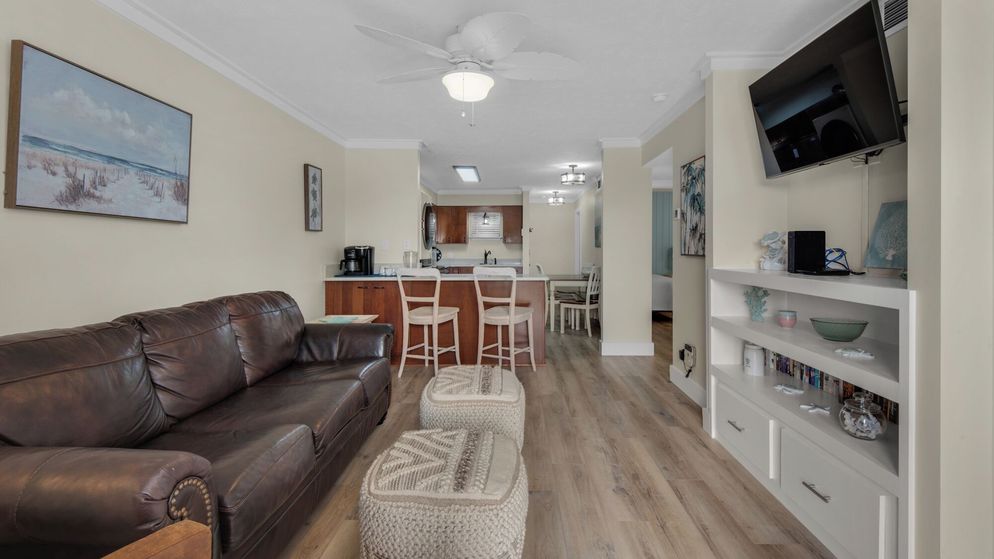 A living room with a brown leather sofa, a white coffee table, and a TV on a white shelf.