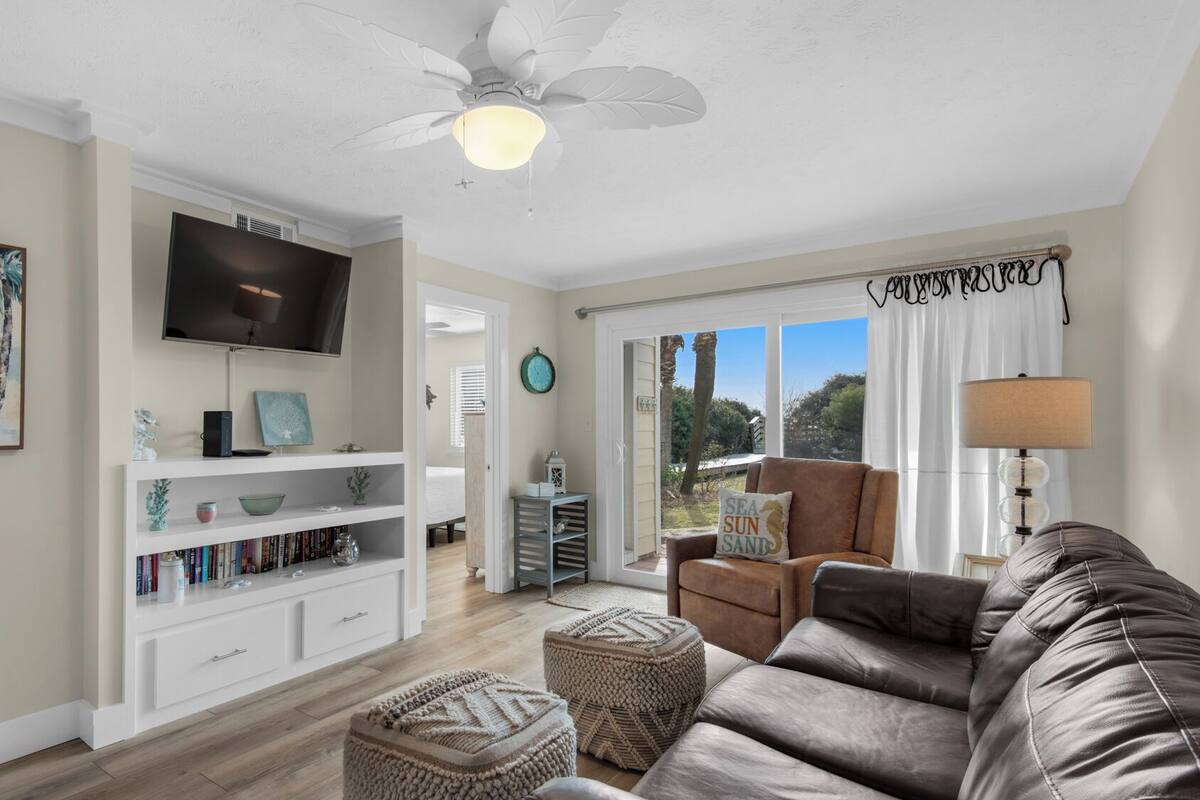 A living room with a flat-screen TV, a bookshelf, a brown leather couch, and a ceiling fan.