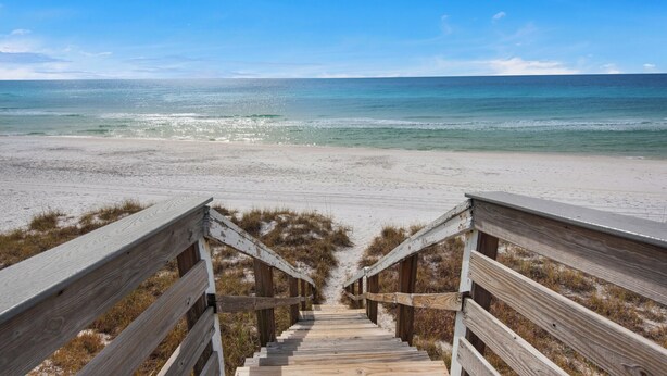Eine Holztreppe führt zu einem Strand mit Blick auf das Meer.
