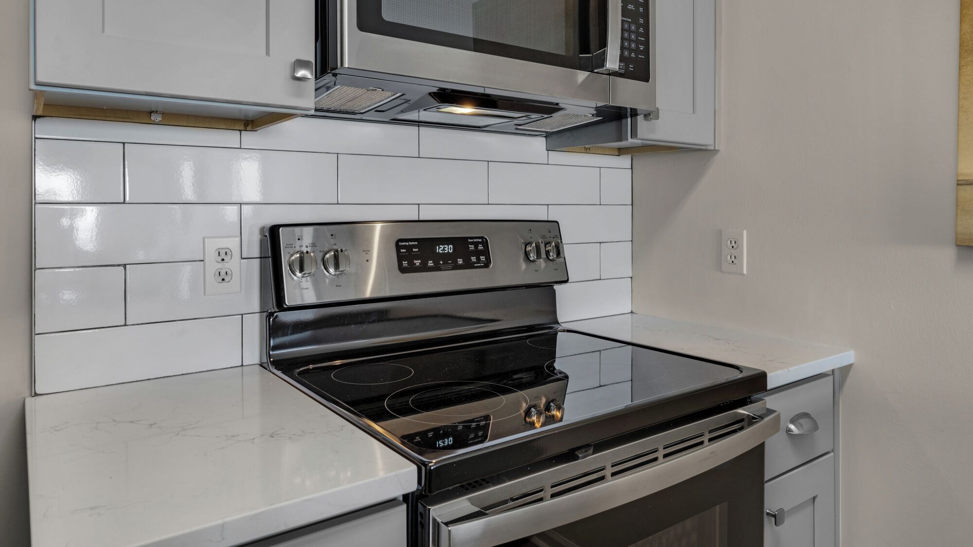 A kitchen with a stainless steel stove, a microwave above it, and white tiled backsplash.