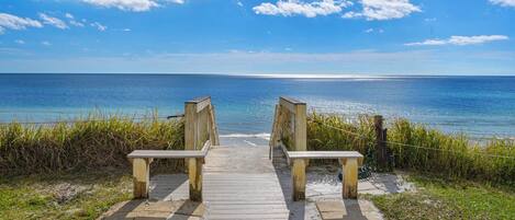 A wooden boardwalk leading to a beach with a clear view of the ocean.