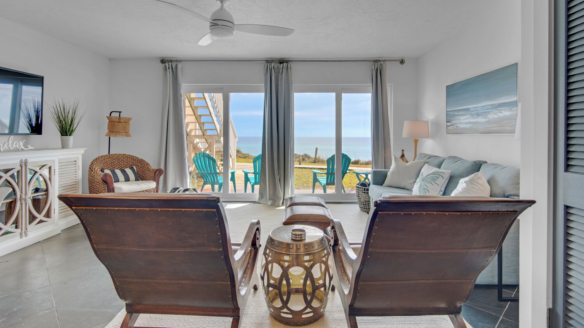 A spacious living room with a large window overlooking the ocean, a comfortable seating area with a sofa and chairs, and a dining table with chairs.