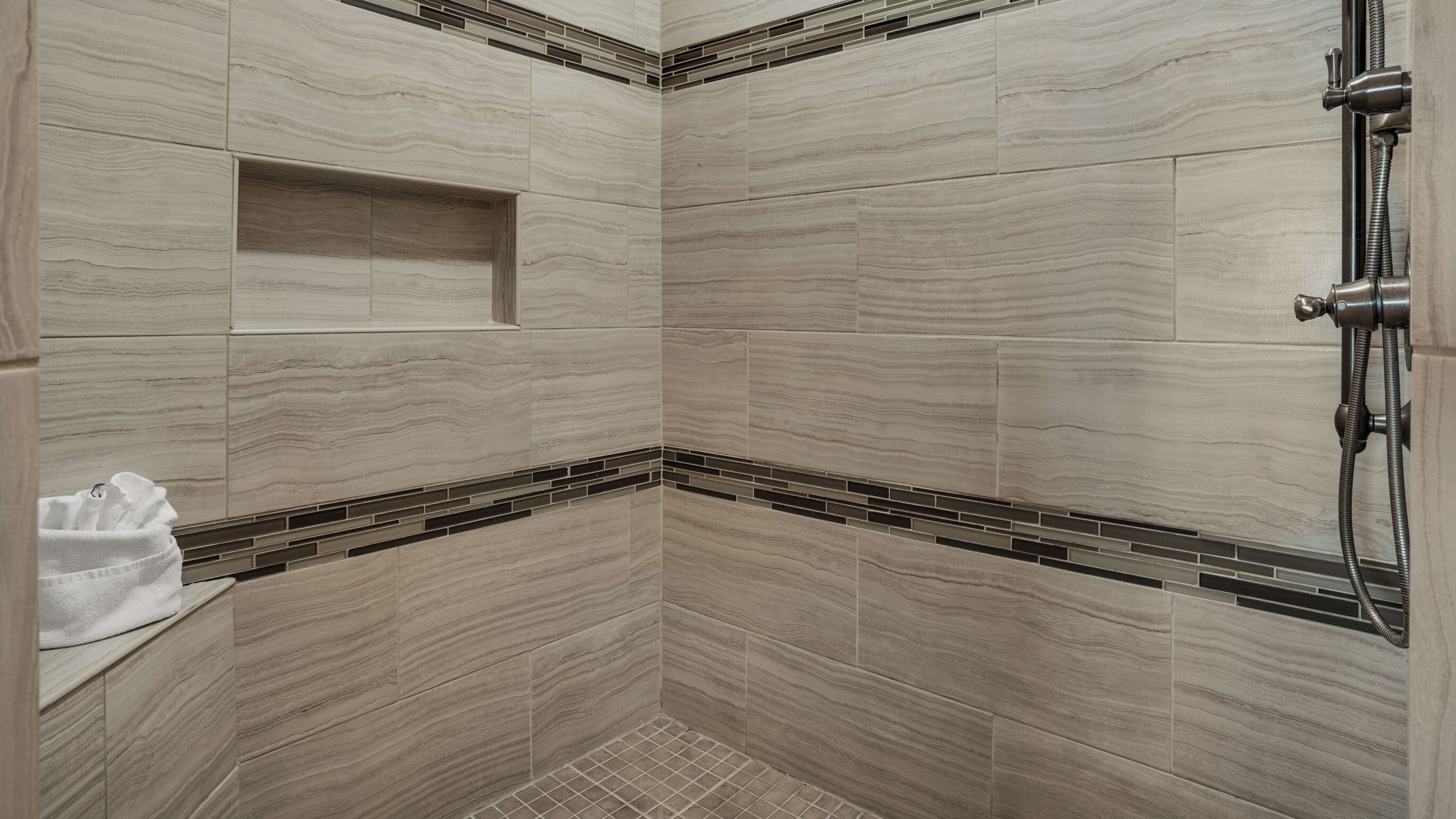 A shower with a built-in shelf and a handheld showerhead.