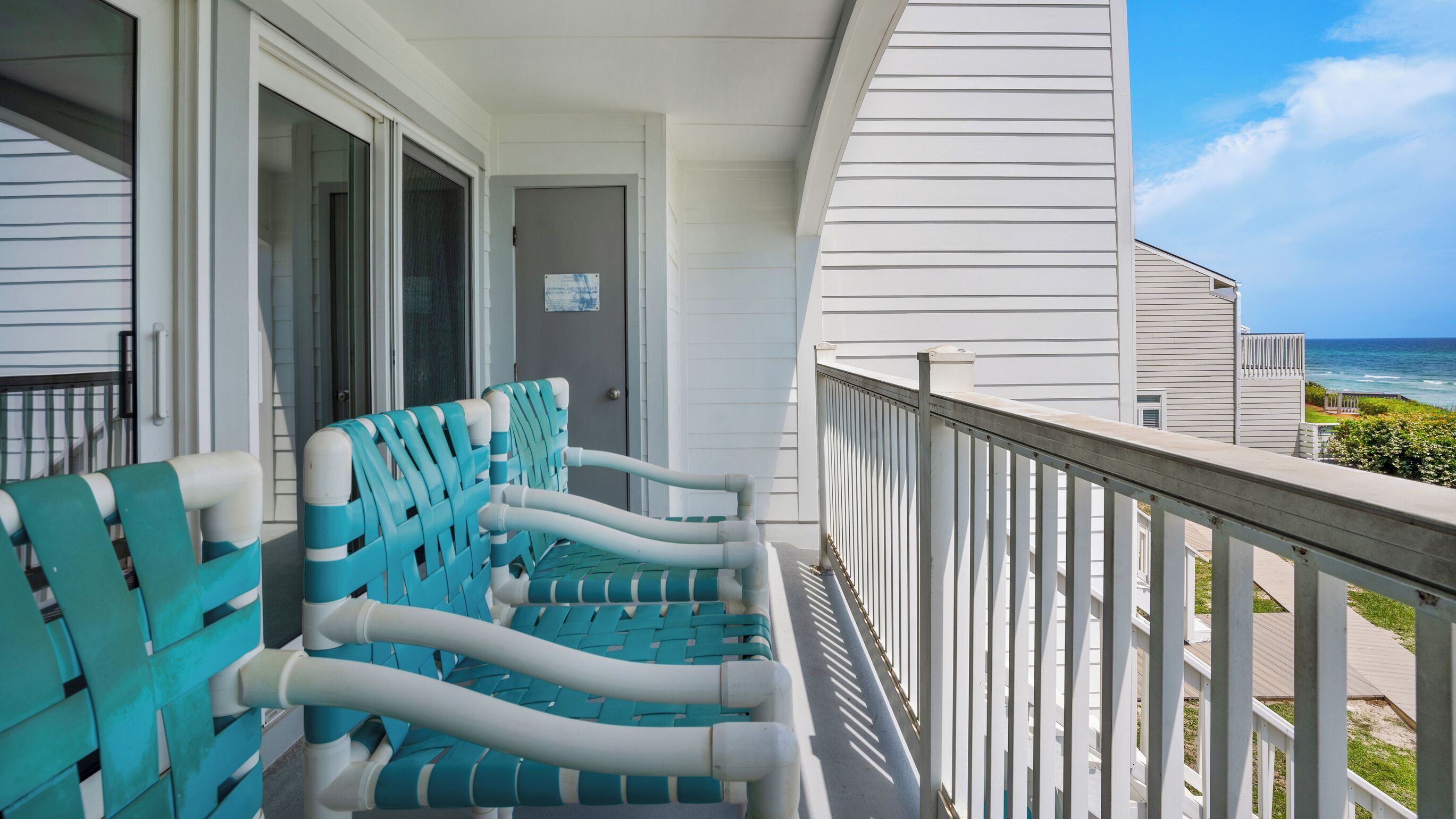 A balcony with two blue and white chairs, a white railing, and a view of the ocean.