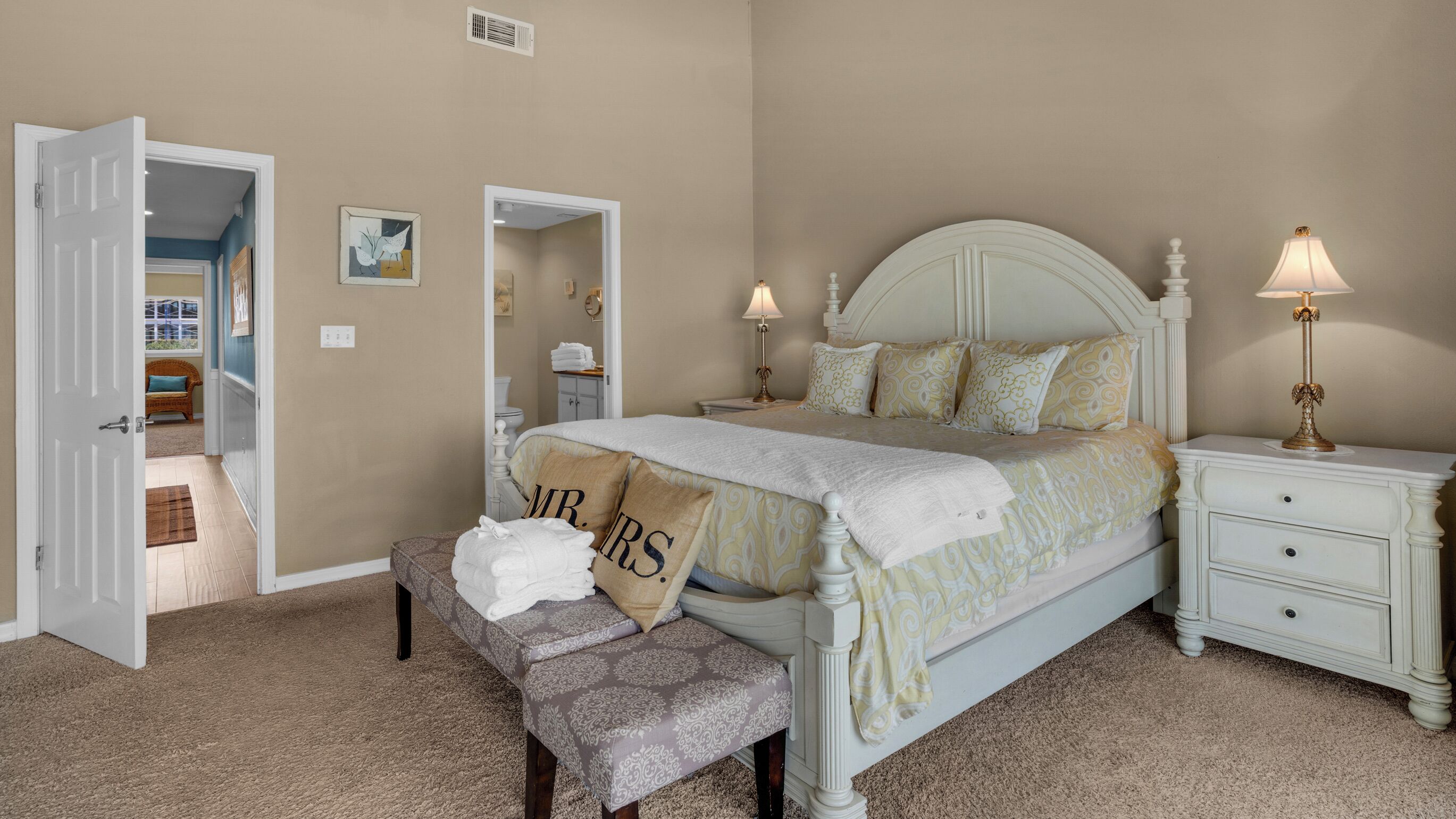 A bedroom with a bed, bedside tables, a bench, and a door leading to another room.