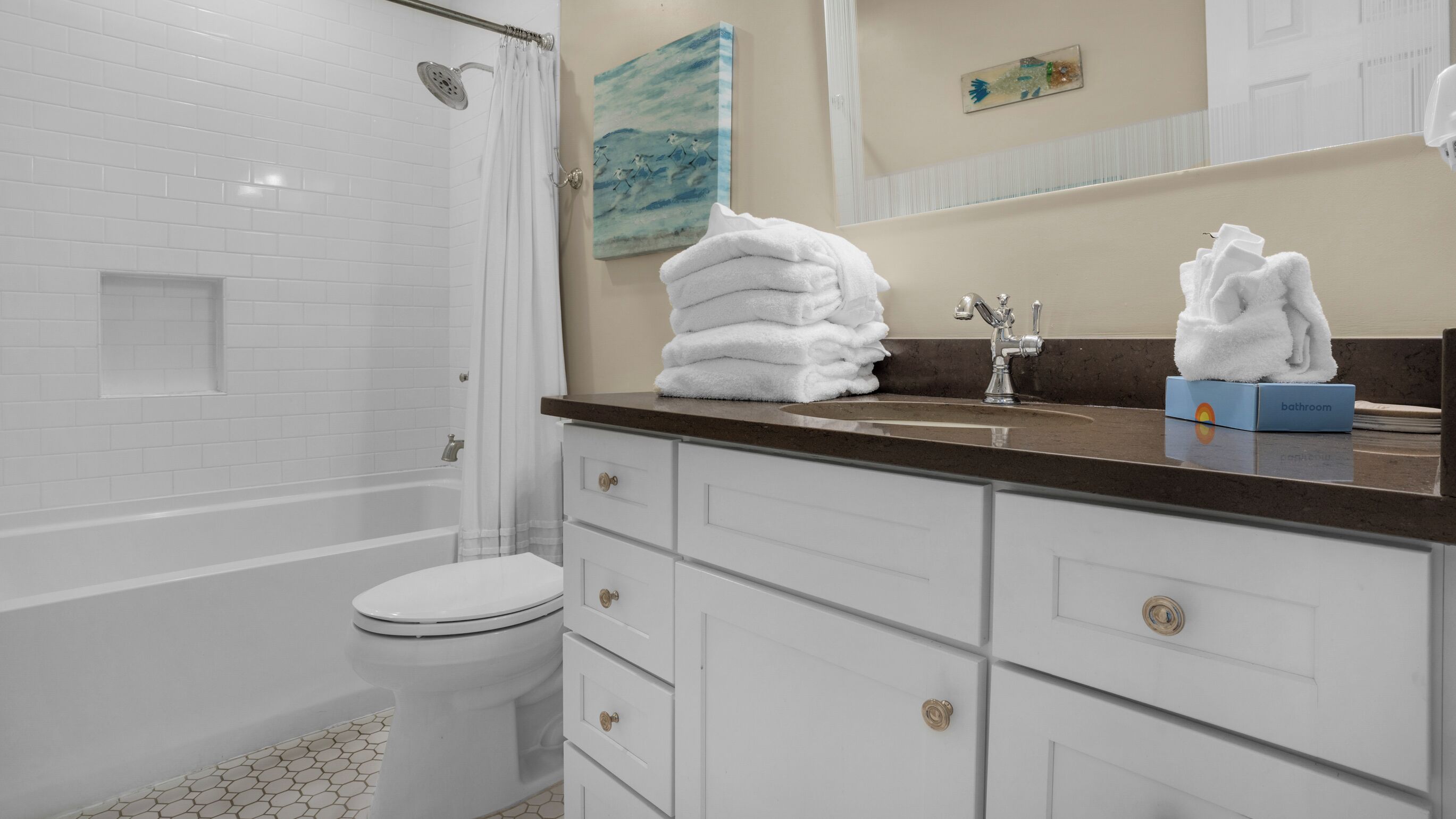 A bathroom with a white toilet, a bathtub, a sink with a towel dispenser, and a mirror.