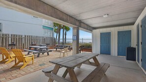 An outdoor patio area with picnic tables and chairs, a covered seating area, and a building with blue doors. - Commodore's Retreat (Santa Rosa Beach)