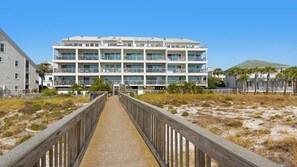 A multi-story hotel with balconies, a boardwalk leading to the entrance, and a sandy beach area. - Commodore's Retreat (Santa Rosa Beach)