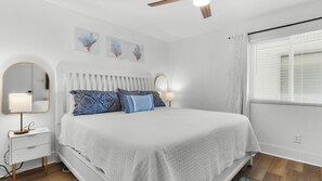 A bedroom with a bed, bedside tables, a mirror, and wall art. - Commodore's Retreat (Santa Rosa Beach)