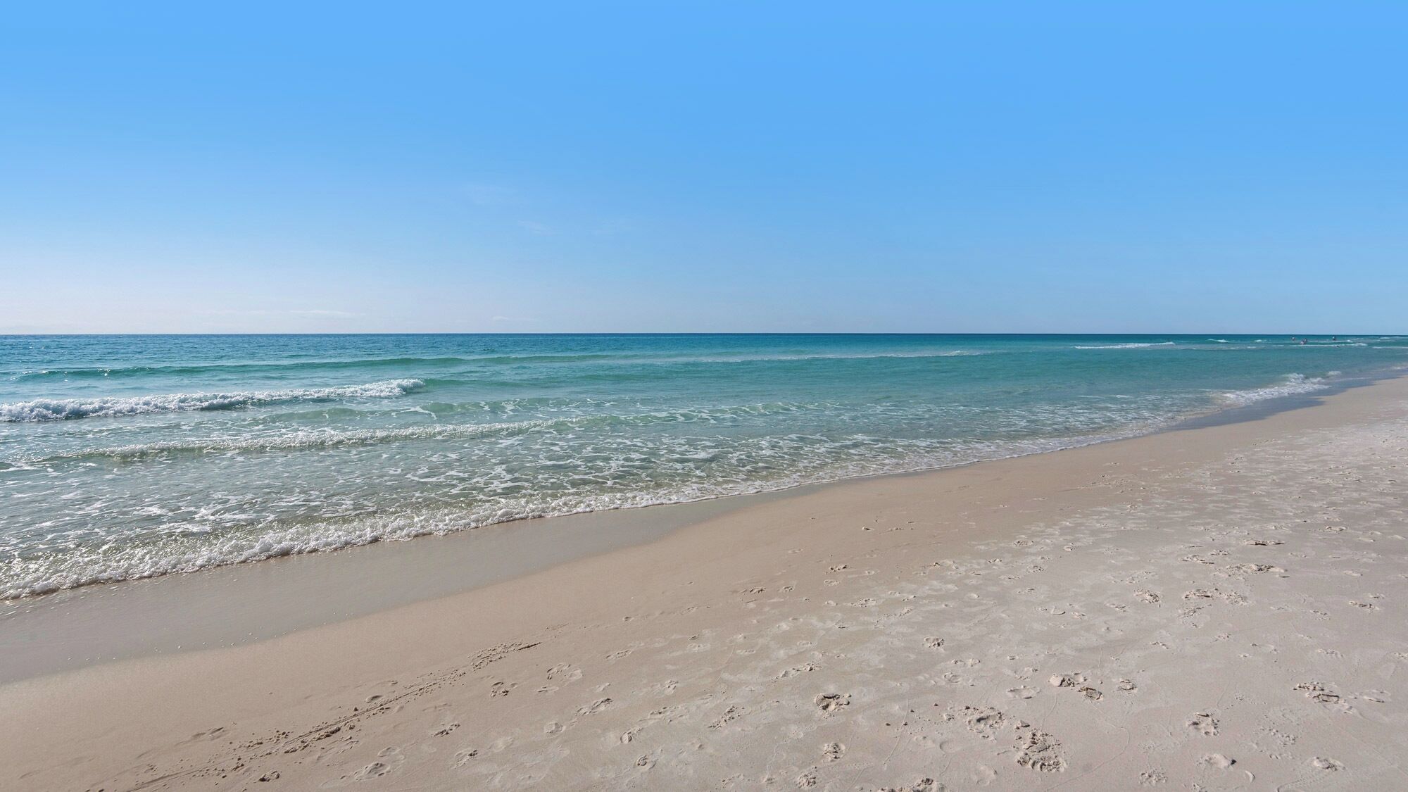 Een strand met heldere lucht en rustige golven.