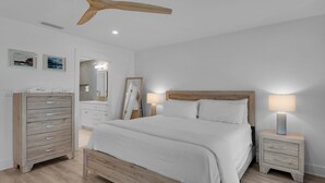 A bedroom with a wooden bed, bedside tables, a dresser, and a ceiling fan.