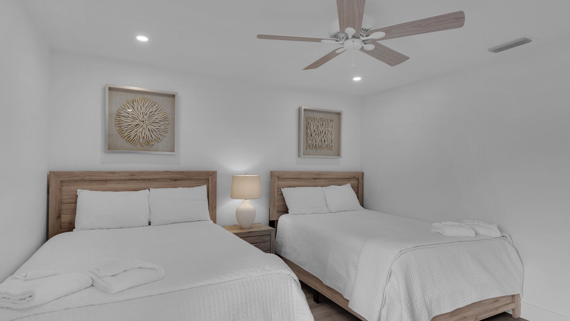 Quarto com duas camas, ventilador de teto e quadros nas paredes.