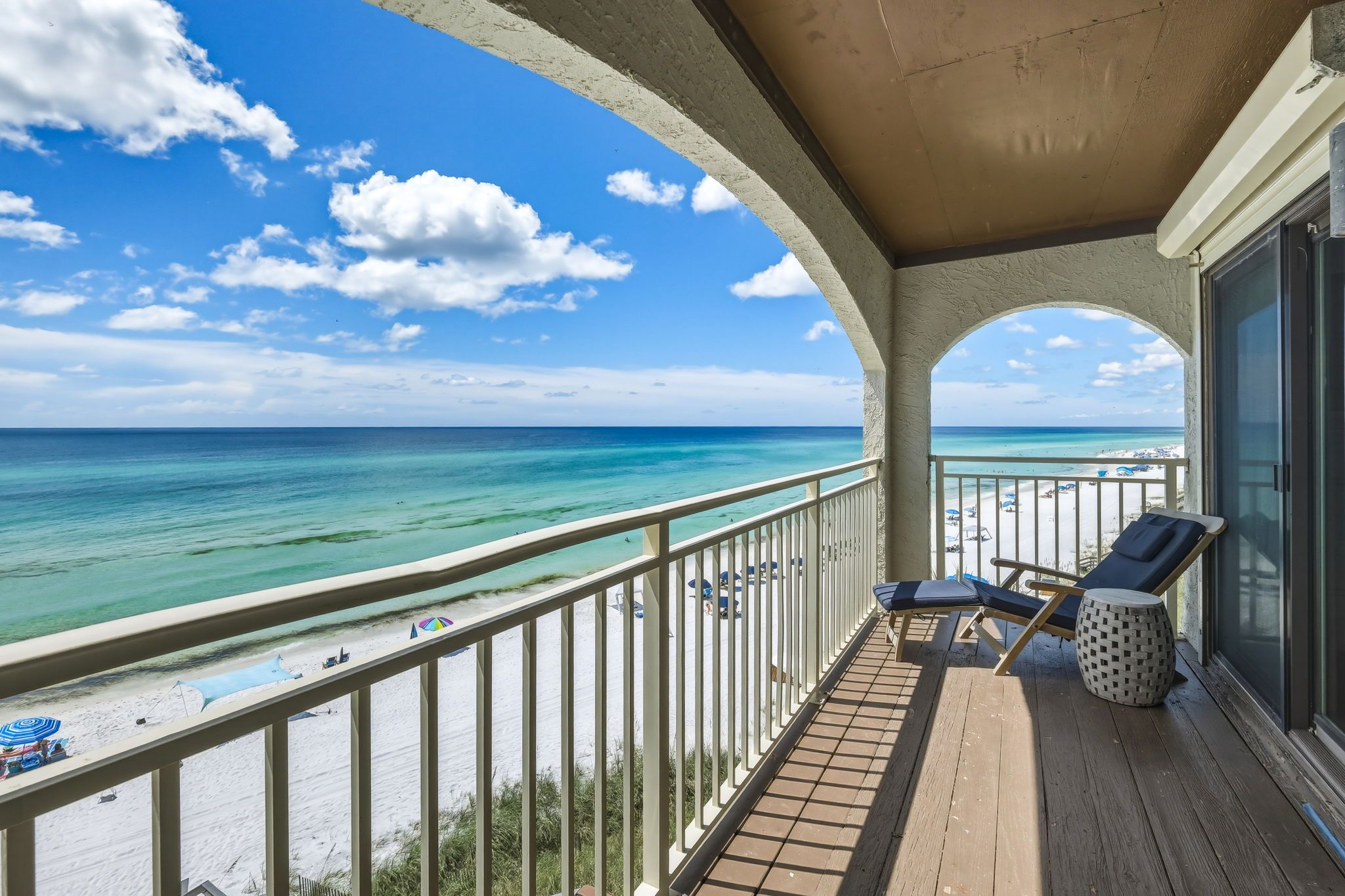 A balcony with a view of the ocean and beach, featuring lounge chairs and a small table.