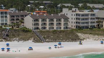 Ein Strandhotel mit mehreren Balkonen, einem Sandstrand und Liegestühlen.