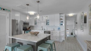 A modern kitchen with white cabinets, stainless steel appliances, and a central island with bar stools. - Dune Villas (Santa Rosa Beach)