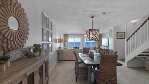 A spacious living area with a large wooden dining table, wicker chairs, and a view of the ocean. - Dune Villas (Santa Rosa Beach)