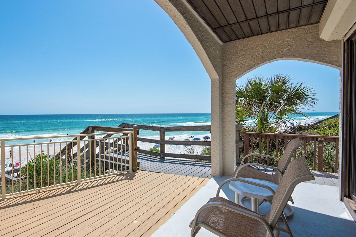 A wooden deck with a view of the beach and ocean.