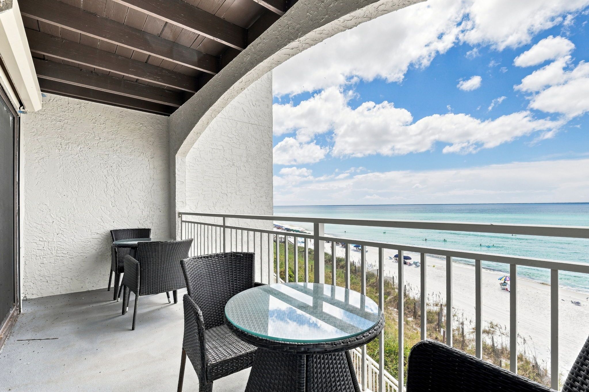 Een balkon met rieten meubels, een glazen tafel en uitzicht op het strand en de oceaan.