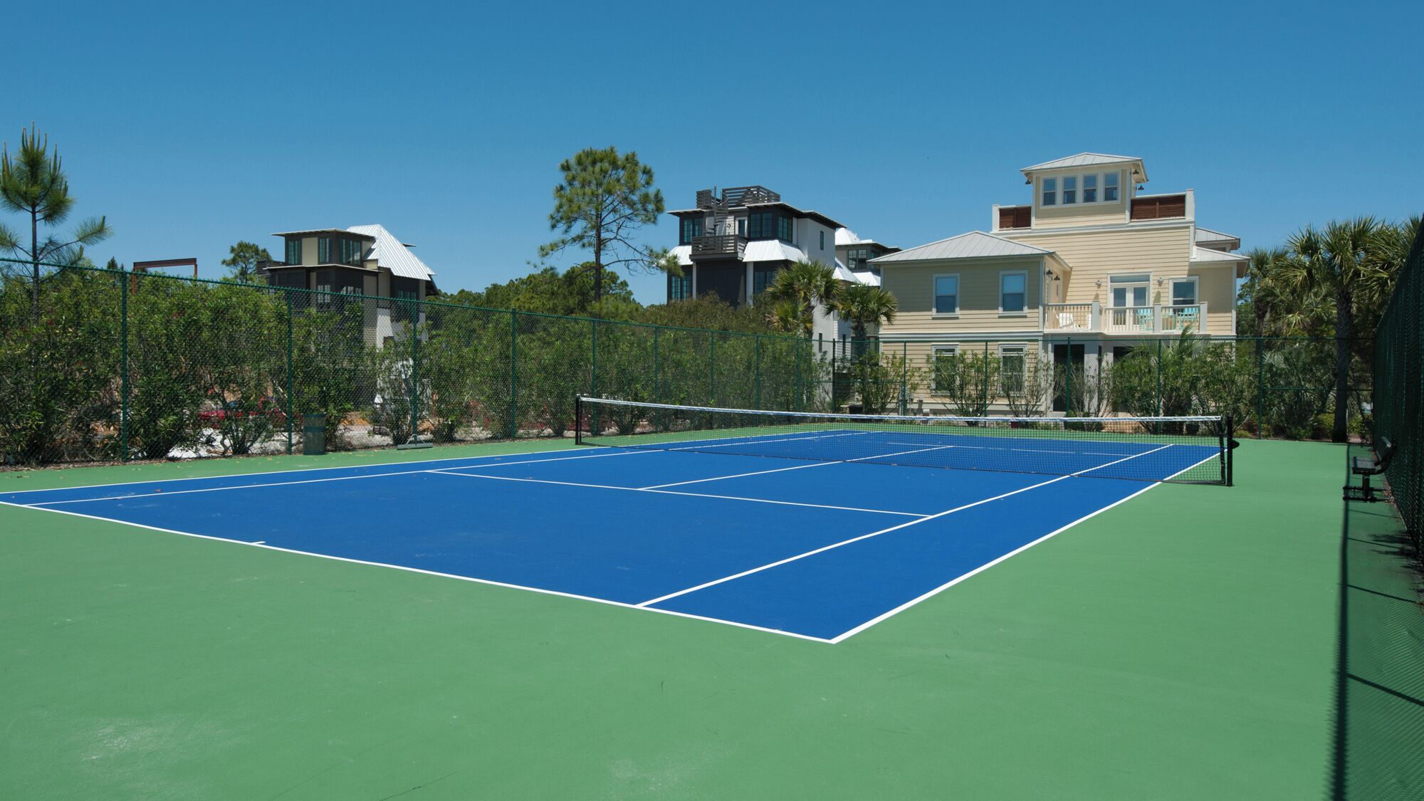 Een buitenbaan voor tennis met een net, omringd door een groene hekken en bomen.