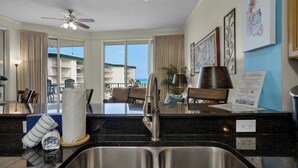 A modern kitchen with a stainless steel sink, a ceiling fan, and a view of the ocean through large windows. - Dunes Of Seagrove (Santa Rosa Beach)