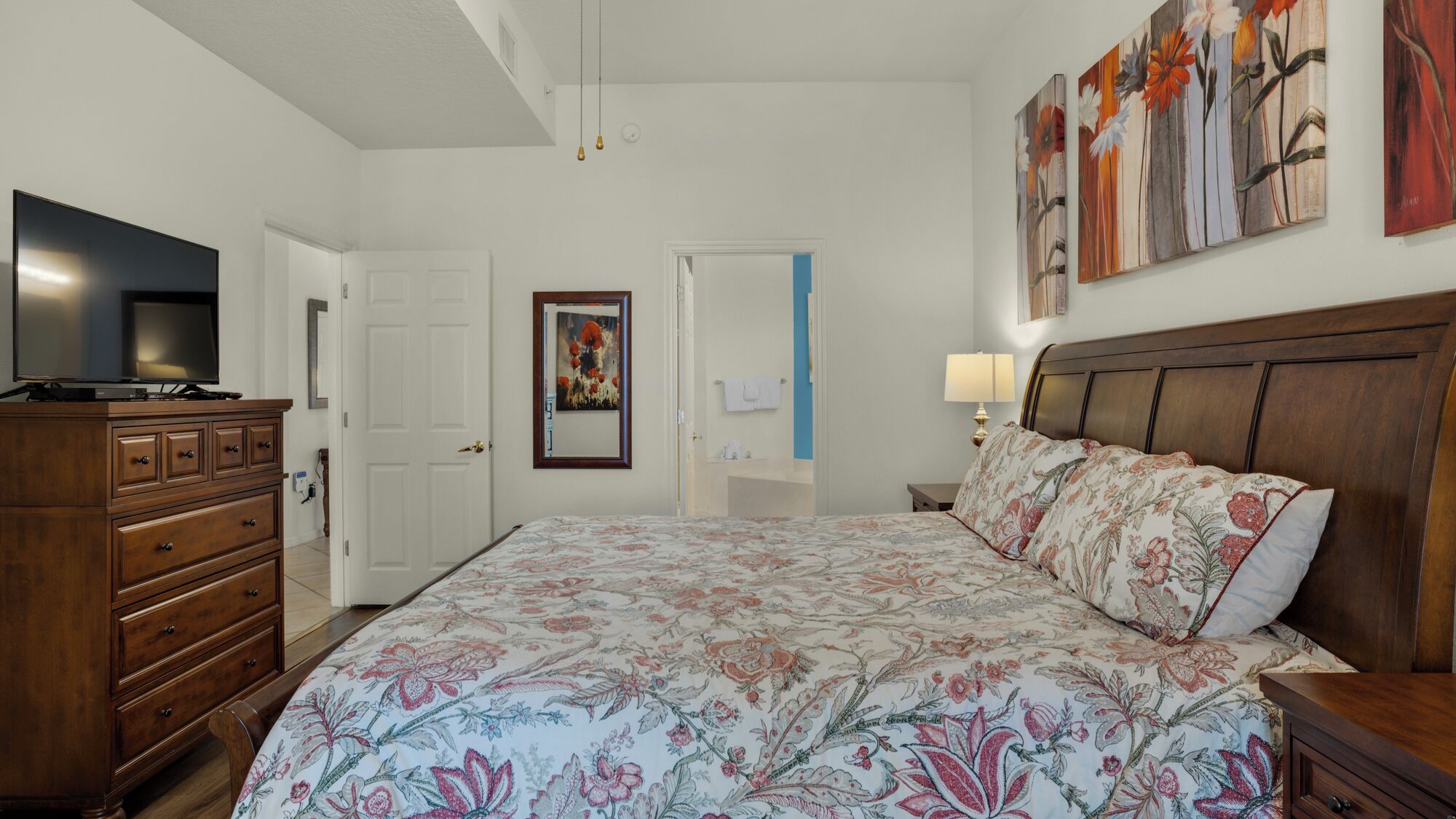 Une chambre à coucher avec un lit, une commode, une télévision et des œuvres d’art accrochées aux murs.