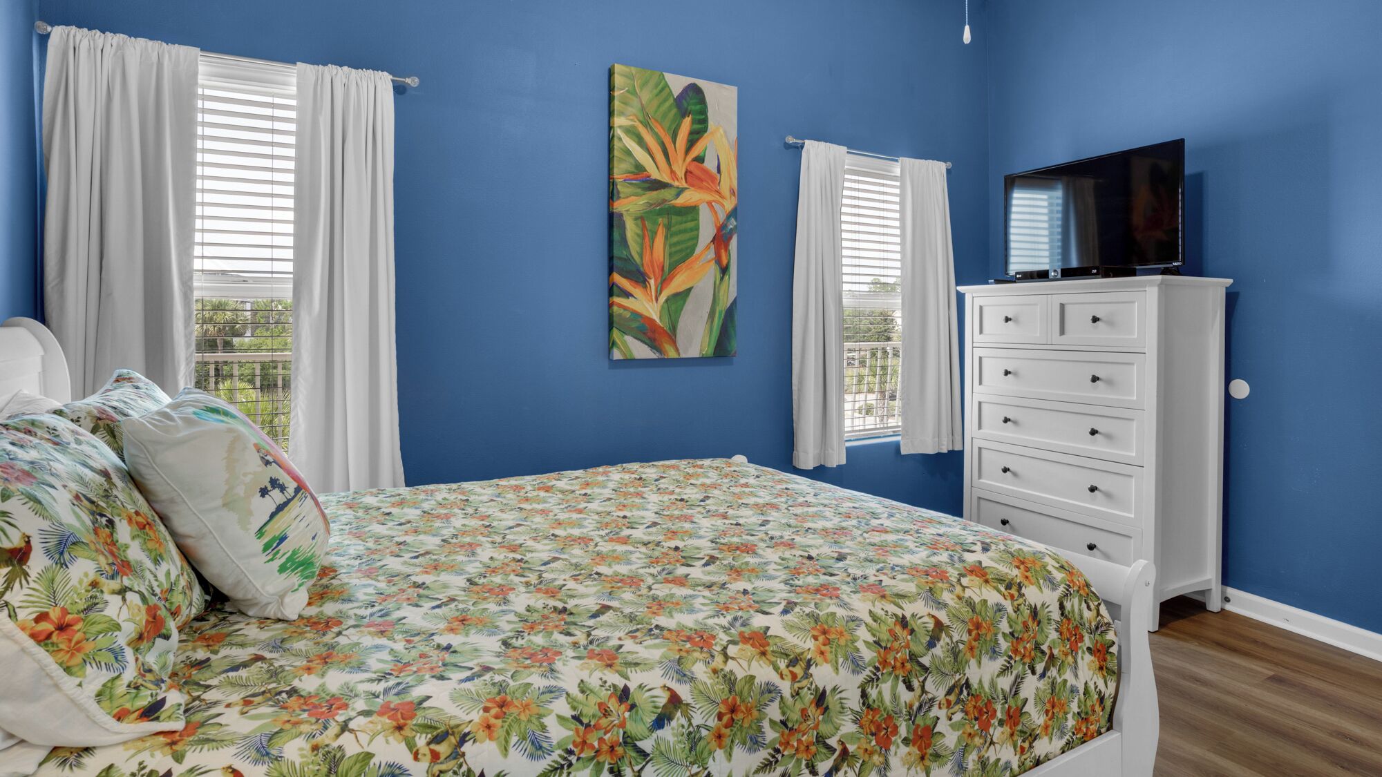 Une chambre à coucher avec un lit, une commode, un téléviseur et un tableau accroché au mur.