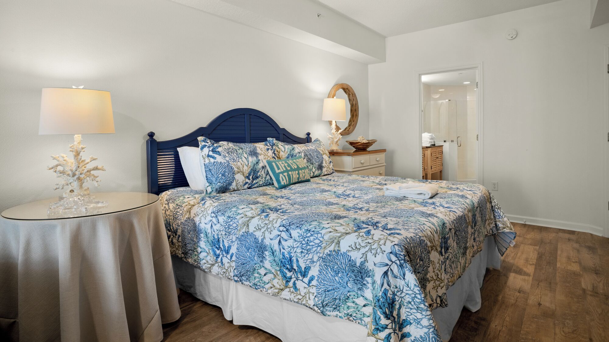 A bedroom with a bed, nightstands, a mirror, and a wooden floor.