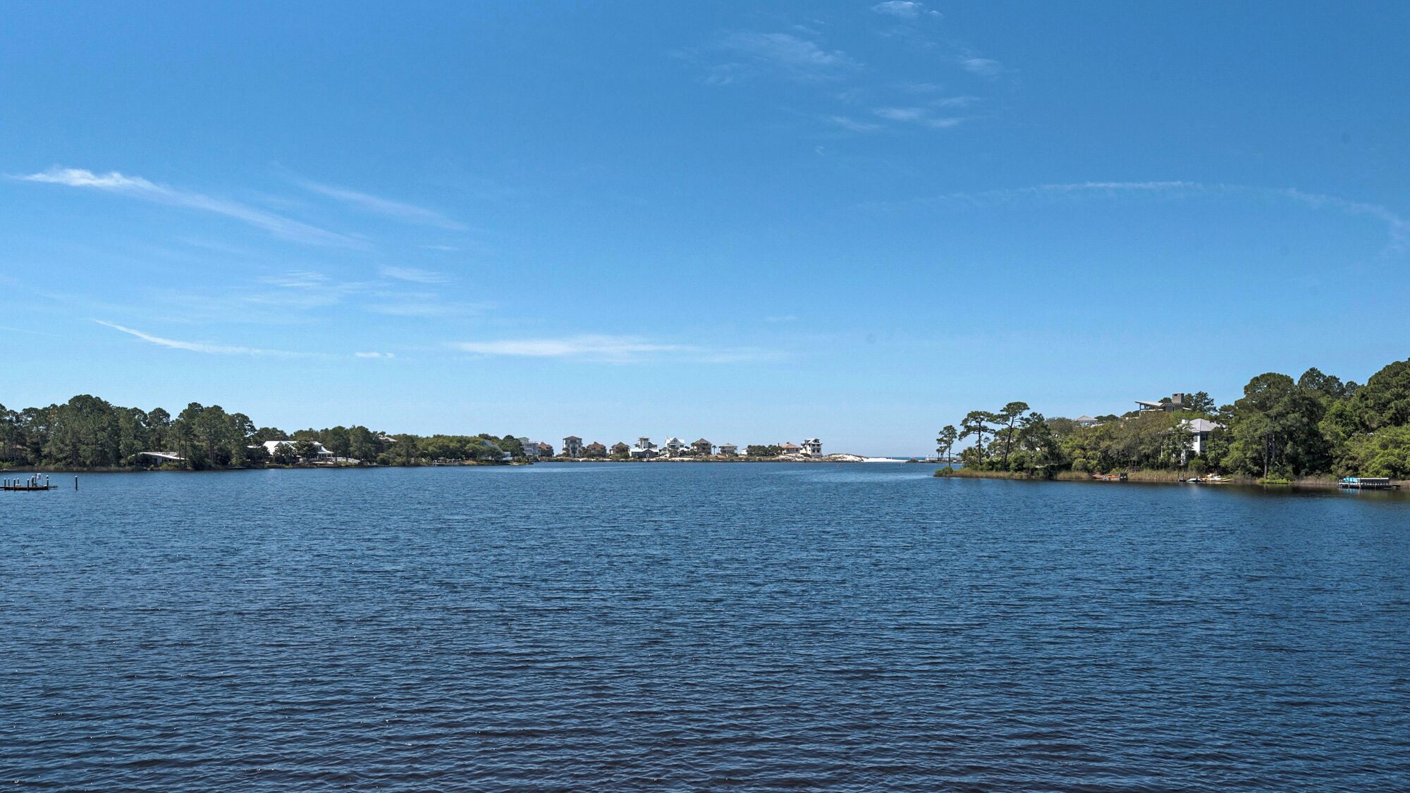 A calm lake with a clear sky, surrounded by trees and buildings on the shore.