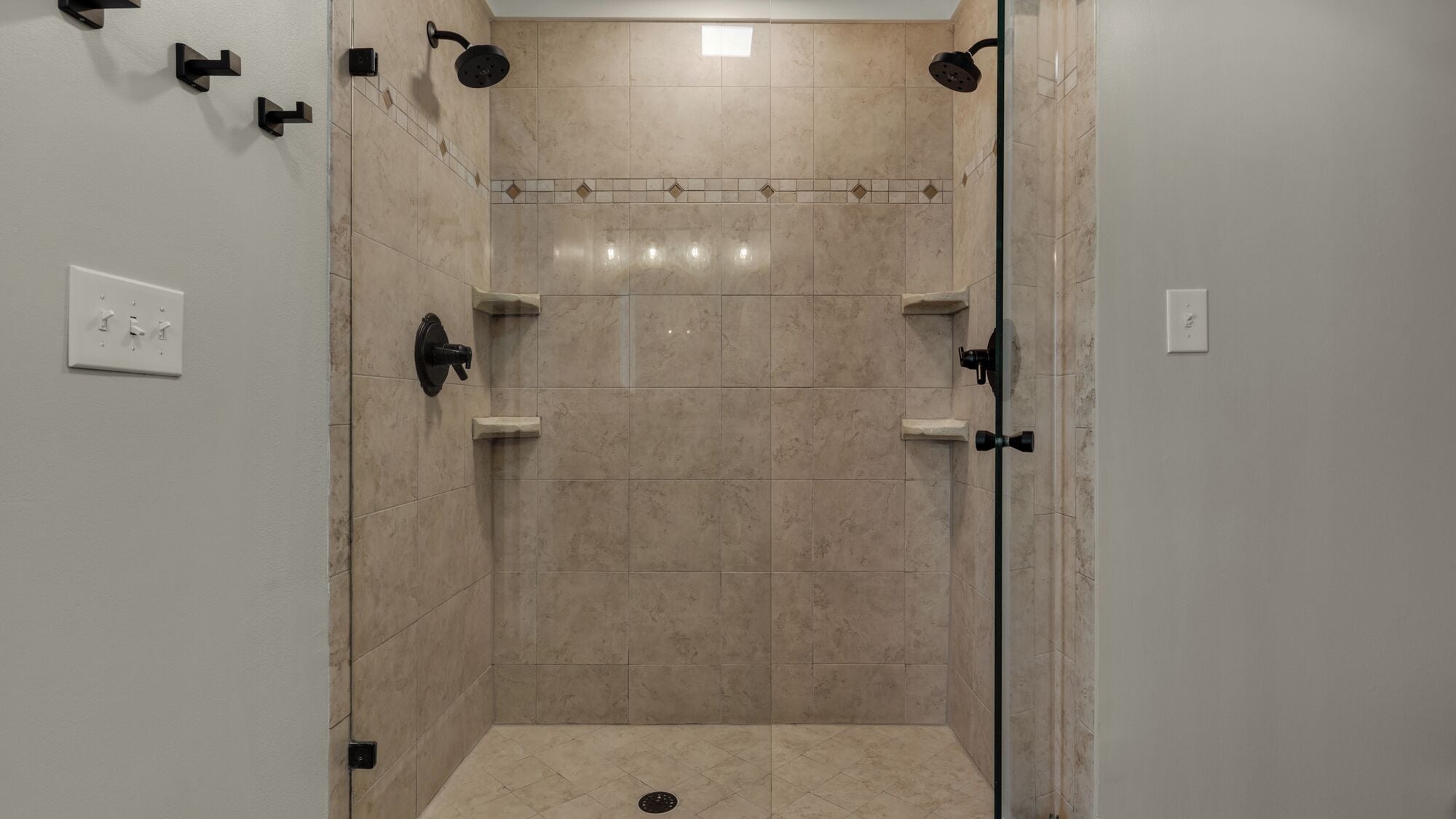 Un espace douche moderne avec des carreaux de couleur beige, des accessoires noirs et un sol carrelé.