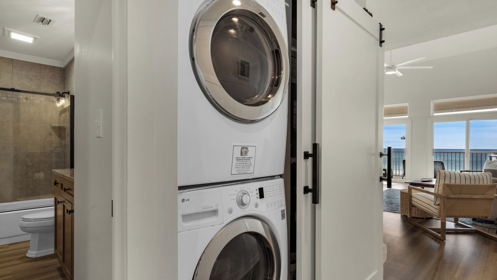A laundry room with stacked washers and dryers, a bathroom with a toilet, and a view of the ocean through large windows.