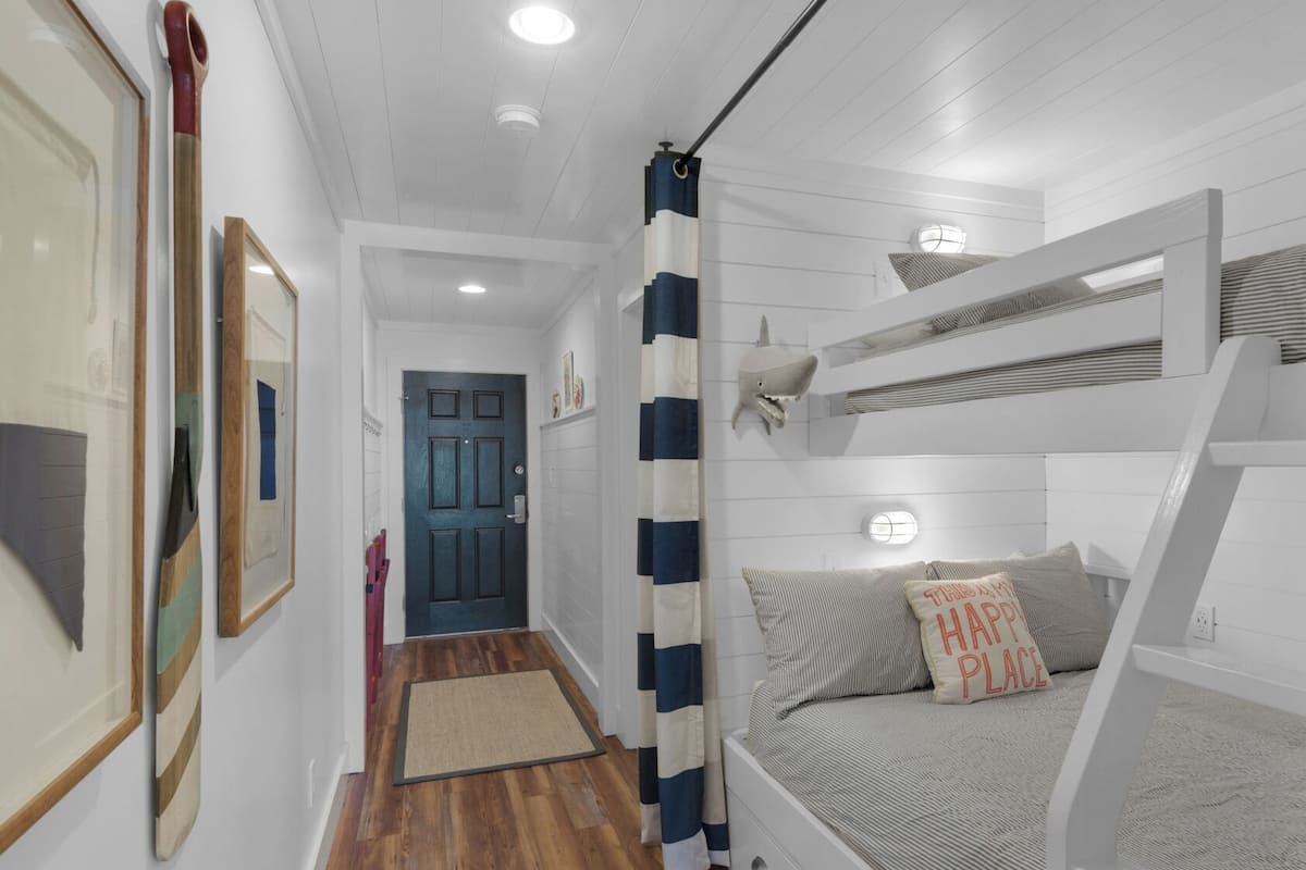 A narrow hallway leading to a bunk bed room with a shark head decoration, a door, and framed pictures on the wall.