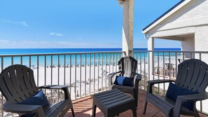 A balcony with two Adirondack chairs and a small table, overlooking a beach with umbrellas and people. - Eastern Shores (Santa Rosa Beach)