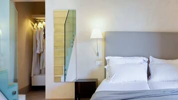 A hotel room with a bed, bedside lamps, a nightstand, a mirror, and a closet with hanging clothes.