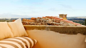 A terrace with a sofa and cushions, overlooking a cityscape and mountains. - Fondaco del Moro (Civitella in Val di Chiana)