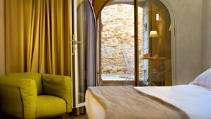 A hotel room with a bed, a yellow armchair, a stone wall, and a window with a lamp. - Fondaco del Moro (Civitella in Val di Chiana)