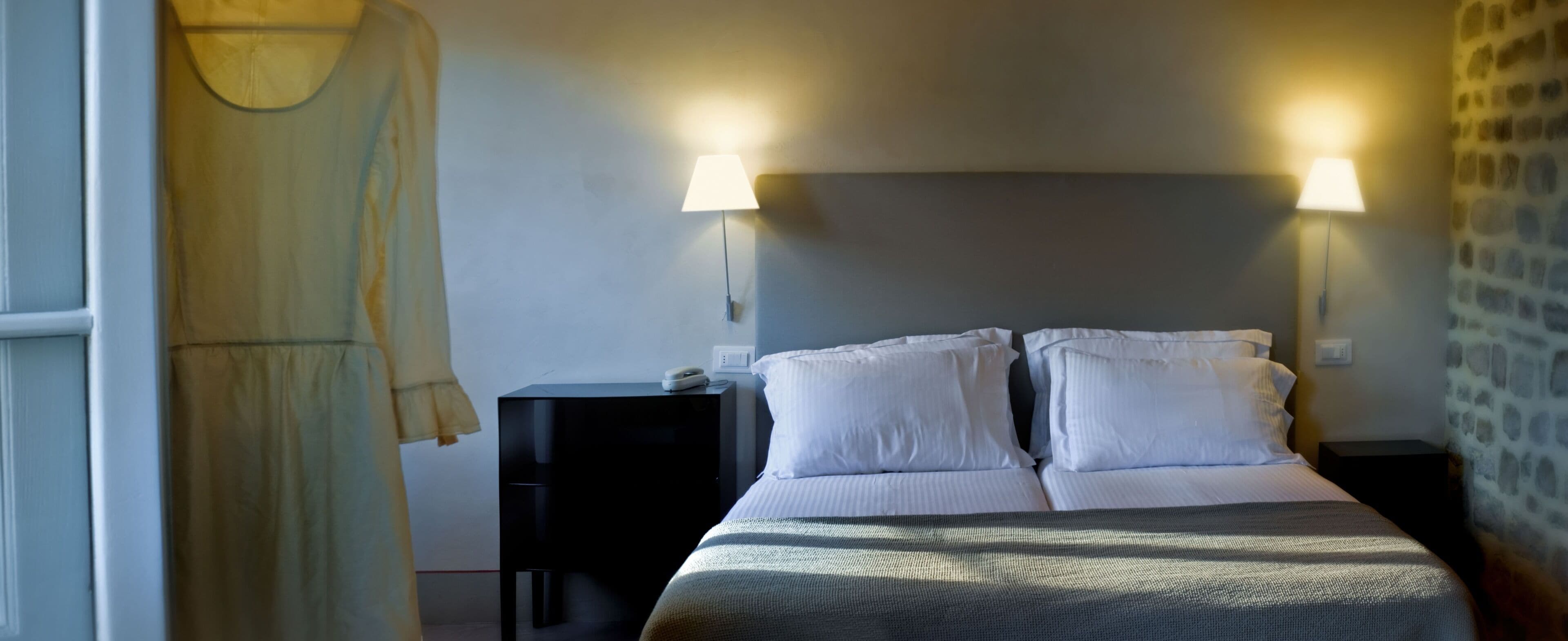 A bedroom with a bed, two bedside tables, a lamp, and a dress on a chair.