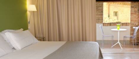 A hotel room with a bed, a lamp, a table with chairs, and a view of a building through a window.