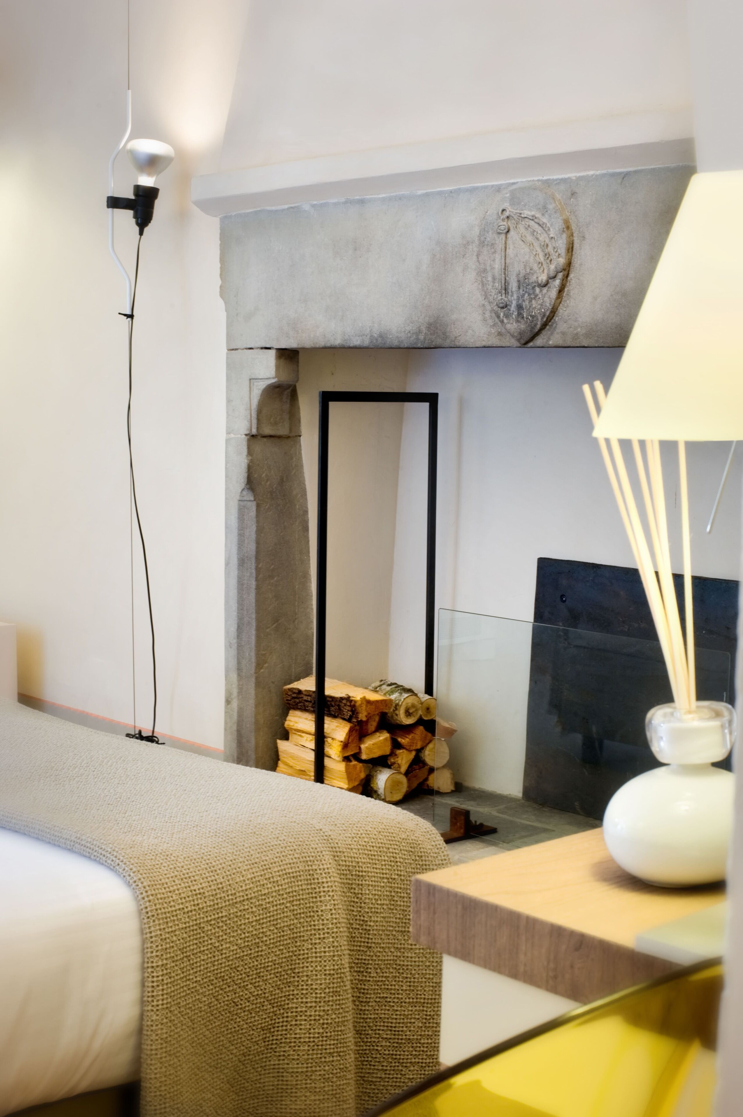 Ein modernes Hotelzimmer mit einem Bett, einem Kamin, einer Lampe und einem Holzstoß.