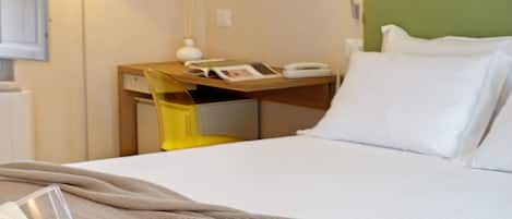 A hotel room with a bed, bedside table, and a breakfast setup including a cup of coffee, a teapot, glasses of orange juice, and a croissant.