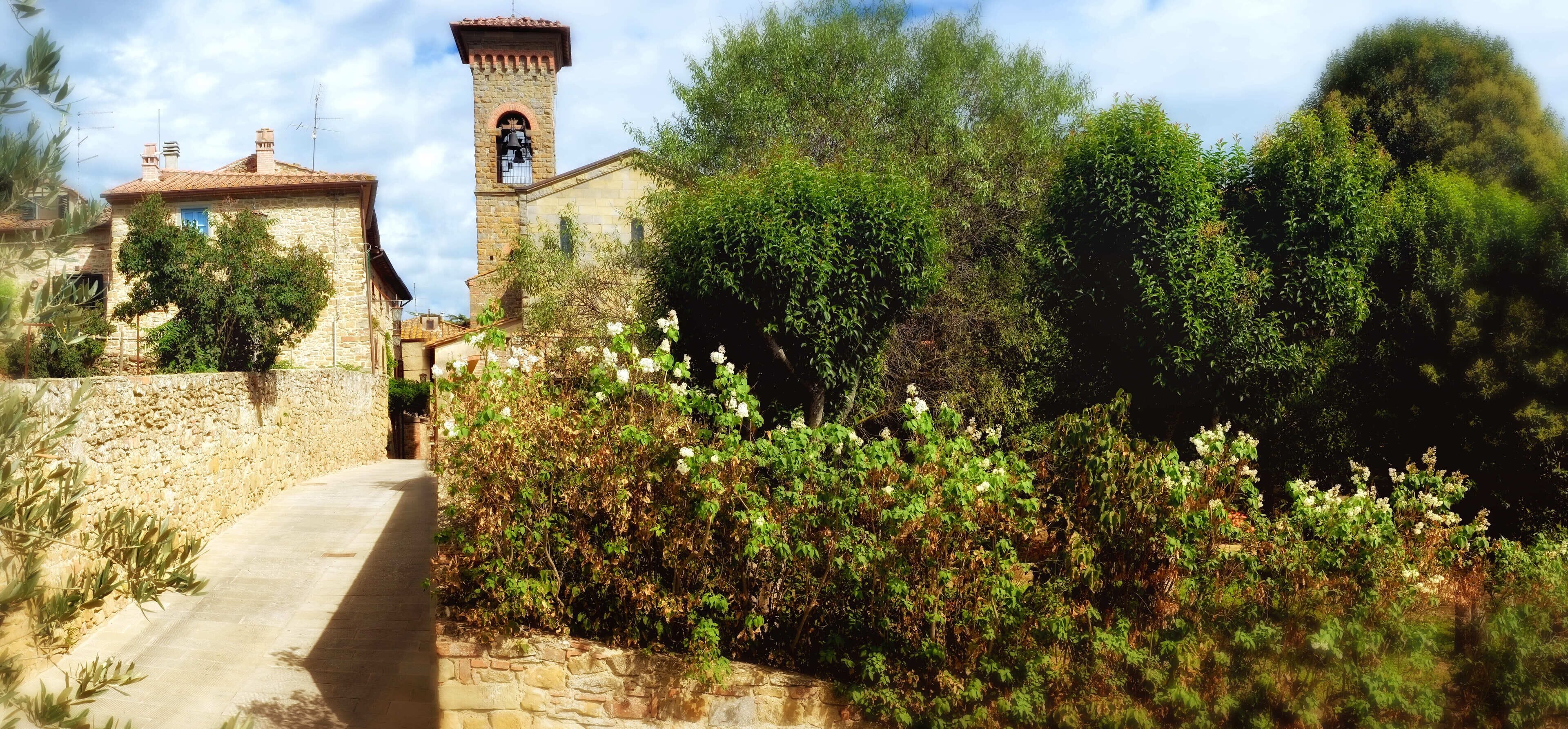A stone building with a bell tower, surrounded by lush greenery and a pathway leading to it.