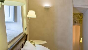 A hotel room with a wooden headboard, a round bedside table with a lamp, and a view of a window and a door.