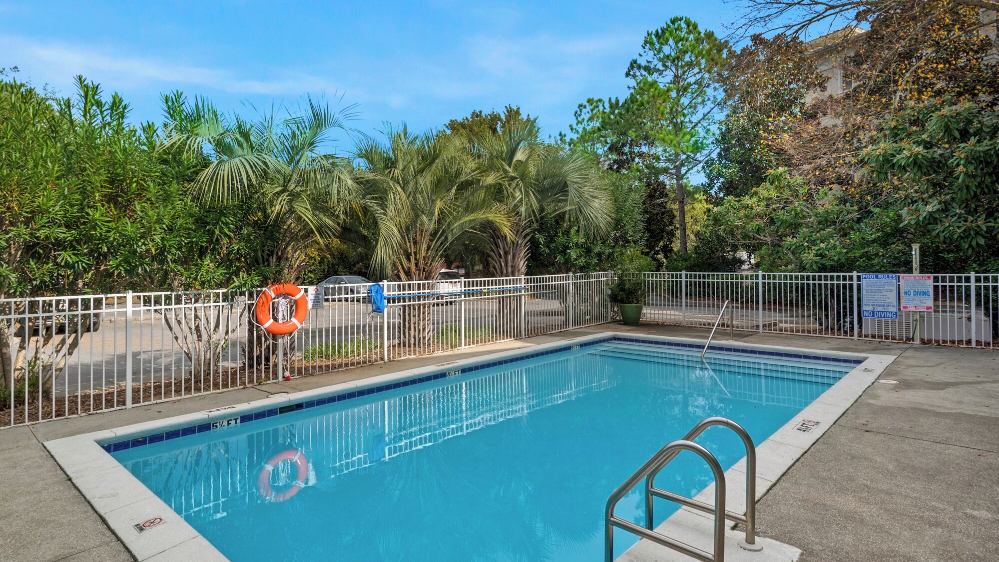 A swimming pool with a white metal fence, a lifebuoy, and pool rules signs.