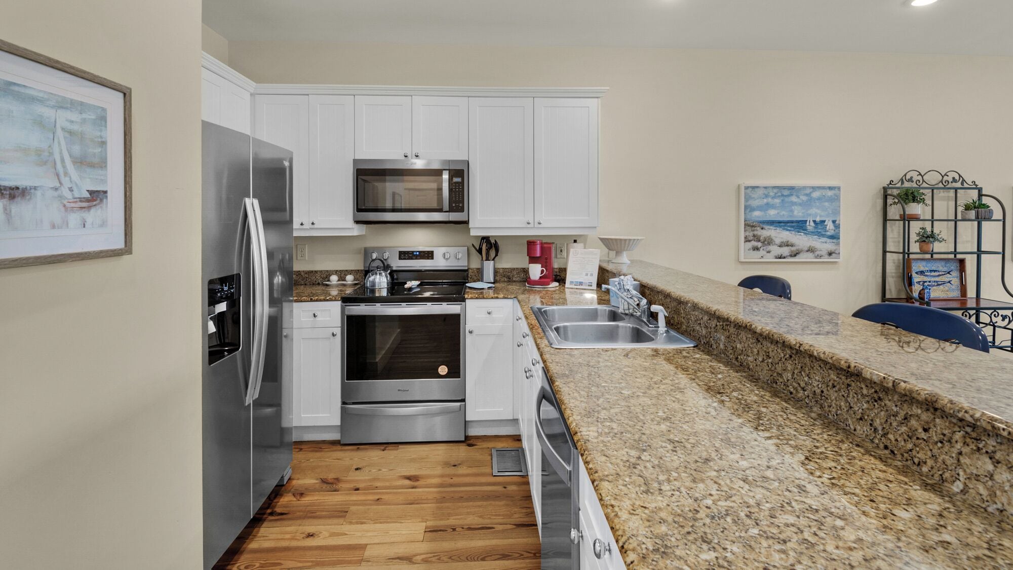 A modern kitchen with stainless steel appliances, white cabinets, granite countertops, and wooden flooring.