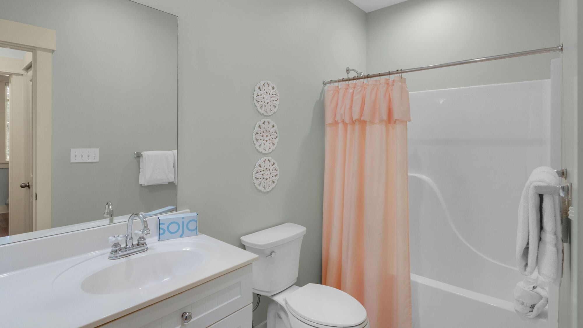 Une salle de bain avec un lavabo, des toilettes et une douche, le tout de couleur blanche. On y trouve également des éléments décoratifs sur les murs et un porte-serviettes.
